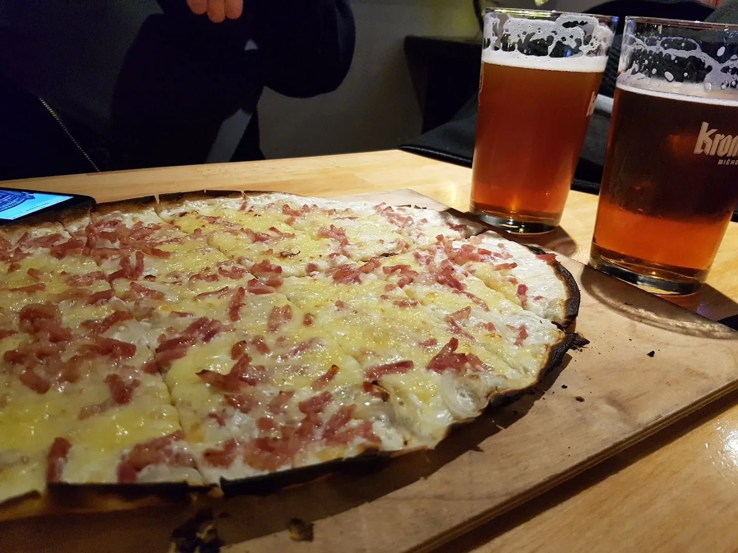 Une tarte flambée sur sa planche, avec deux bières